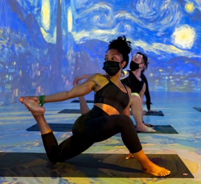 
                              A young woman sitting on a yoga mat performs yoga posses underneath a projection of Van Gogh's 'The Starry Night'